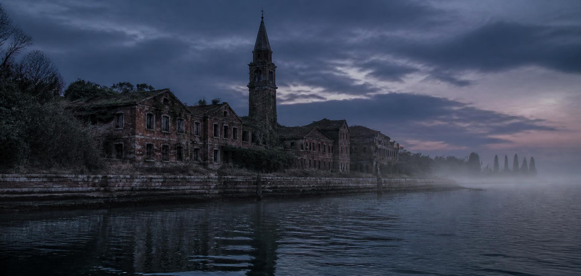 The abandoned brick asylum and bell tower of Poveglia island across the misty Venetian lagoon at dusk
